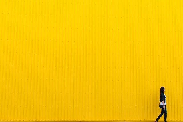 Woman walking by a bright, sunny yellow wall