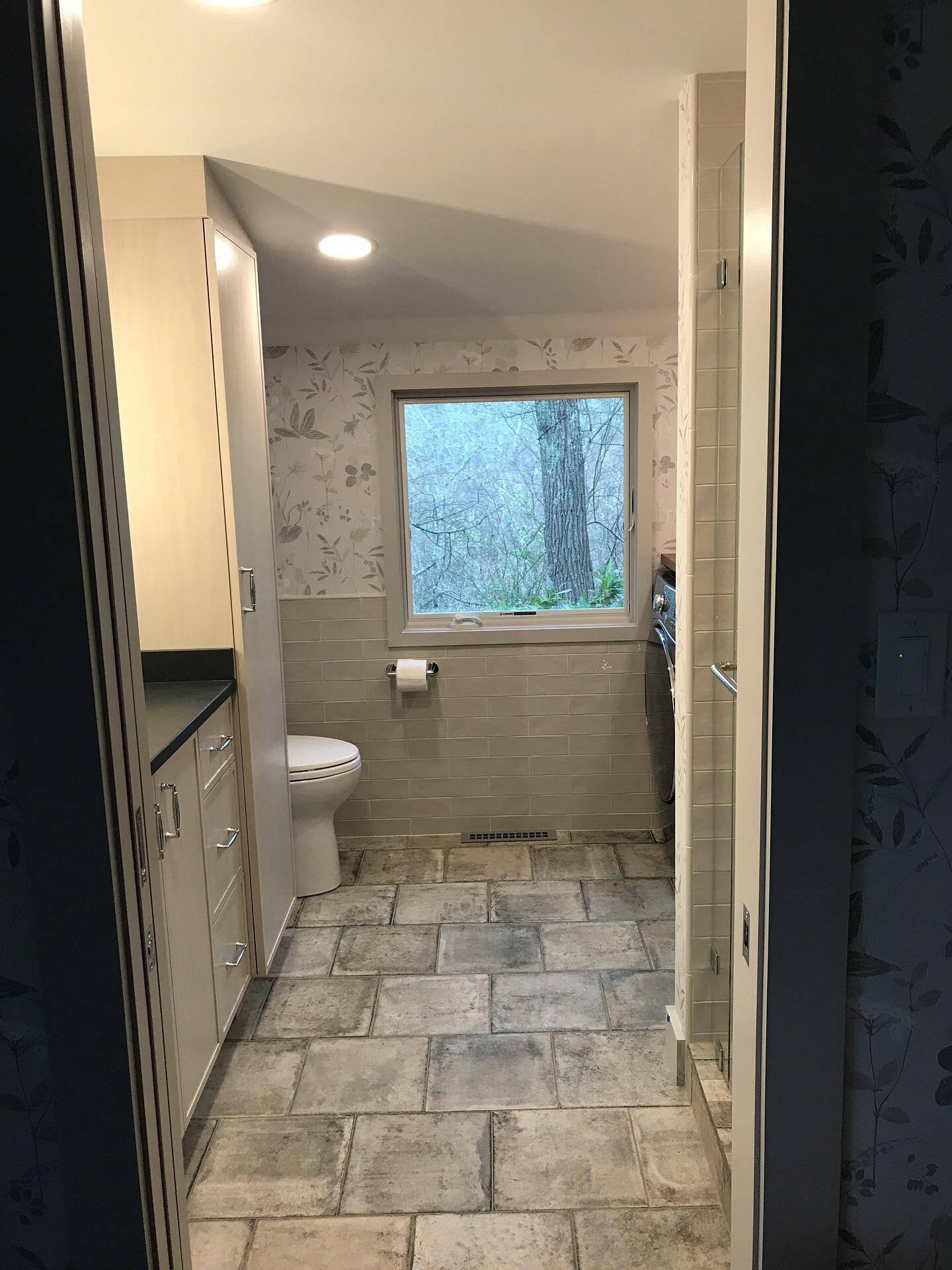 Bright bathroom with stone tile flooring and natural light from a large window in a Cape Cod home remodeled by @designREMODEL