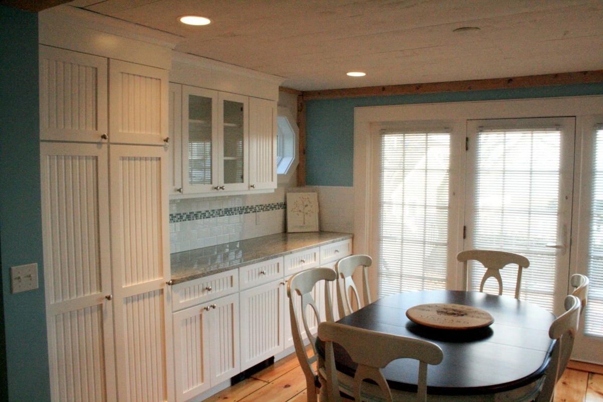 Cozy dining area with white cabinetry and beadboard panels in a Cape Cod kitchen remodel by @designREMODEL